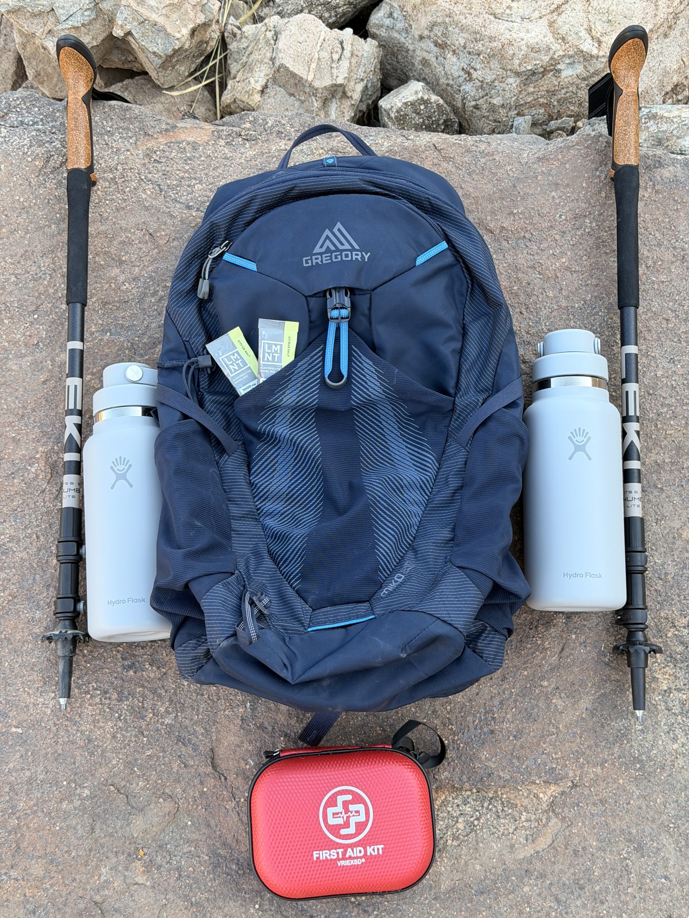 Palm Springs Adventure Club gear kit: Gregory daypack, Leki trekking poles, two Hydro Flask bottles, and first aid kit laid out on desert rock