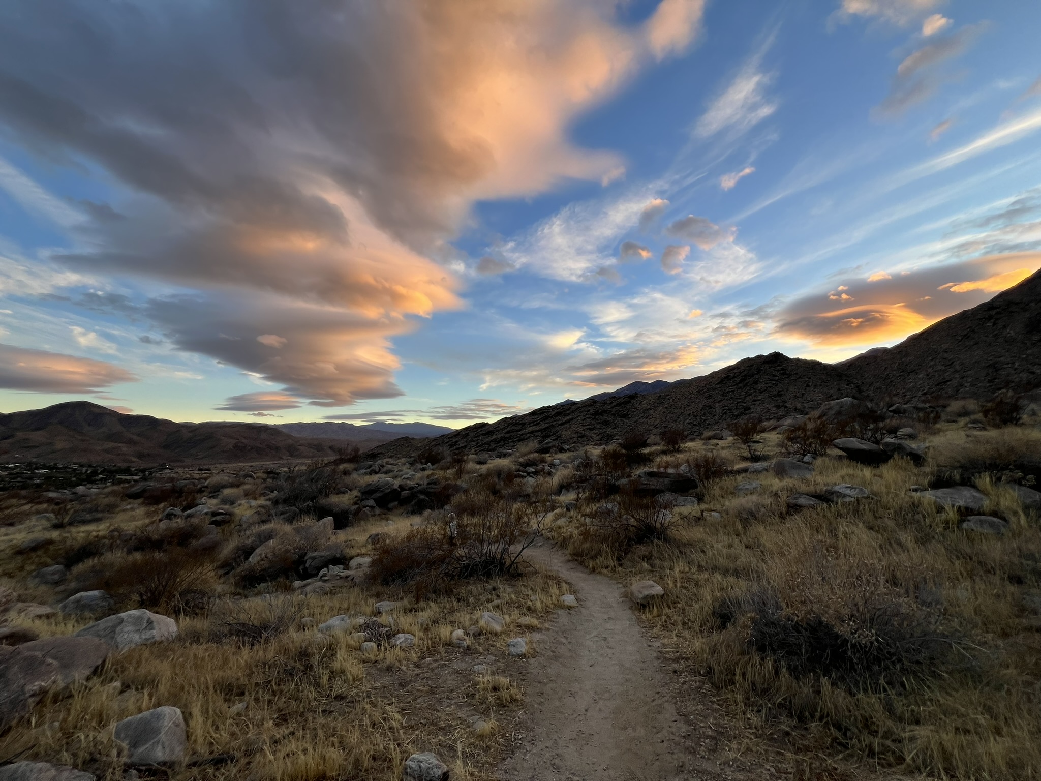 Desert trail at sunset in Palm Springs, California — the San Jacinto mountains glow amber and coral as golden light crosses the valley