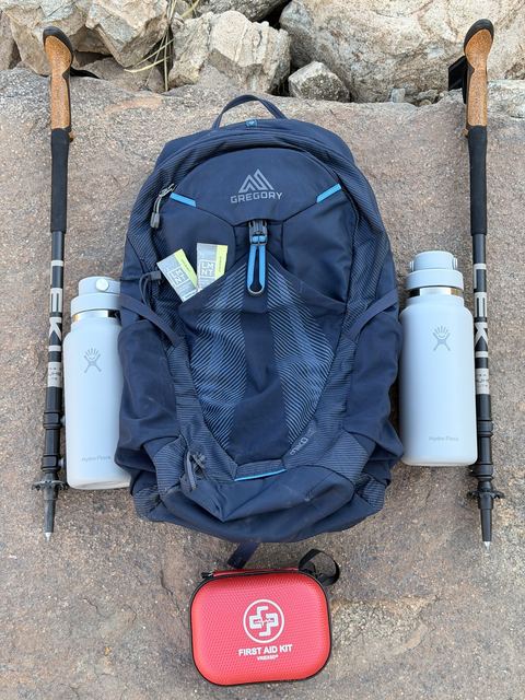 Palm Springs Adventure Club gear kit: Gregory daypack, Leki trekking poles, two Hydro Flask bottles, and first aid kit laid out on desert rock